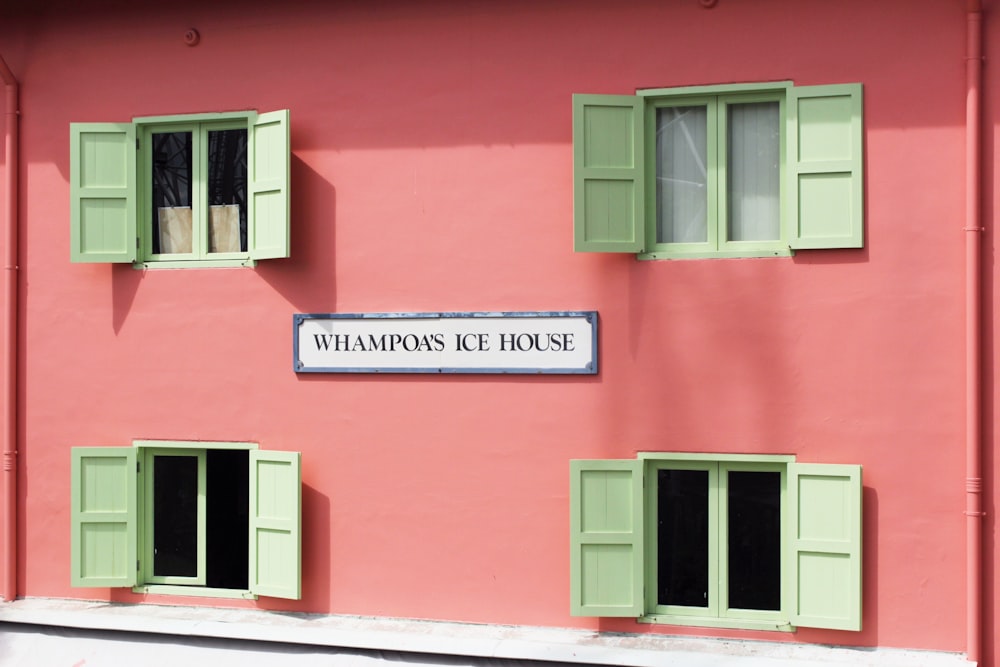 a pink building with green shutters and a sign