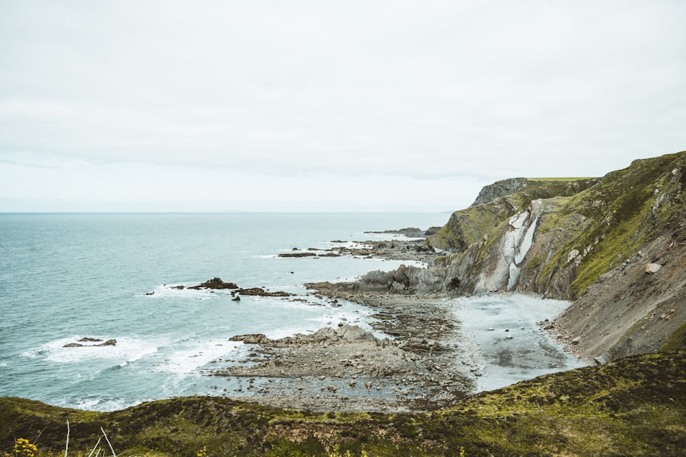 green grass covered mountain beside sea during daytime