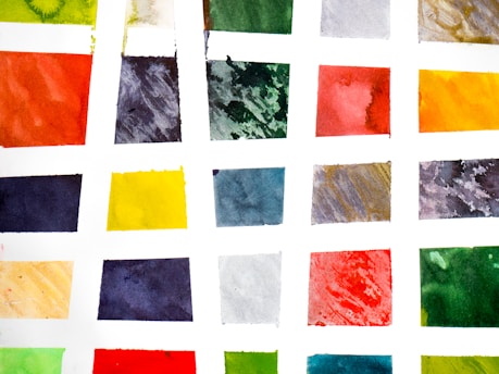 An arrangement of watercolor swatches in a grid pattern with a variety of vibrant colors, each square containing a different hue on a white background.