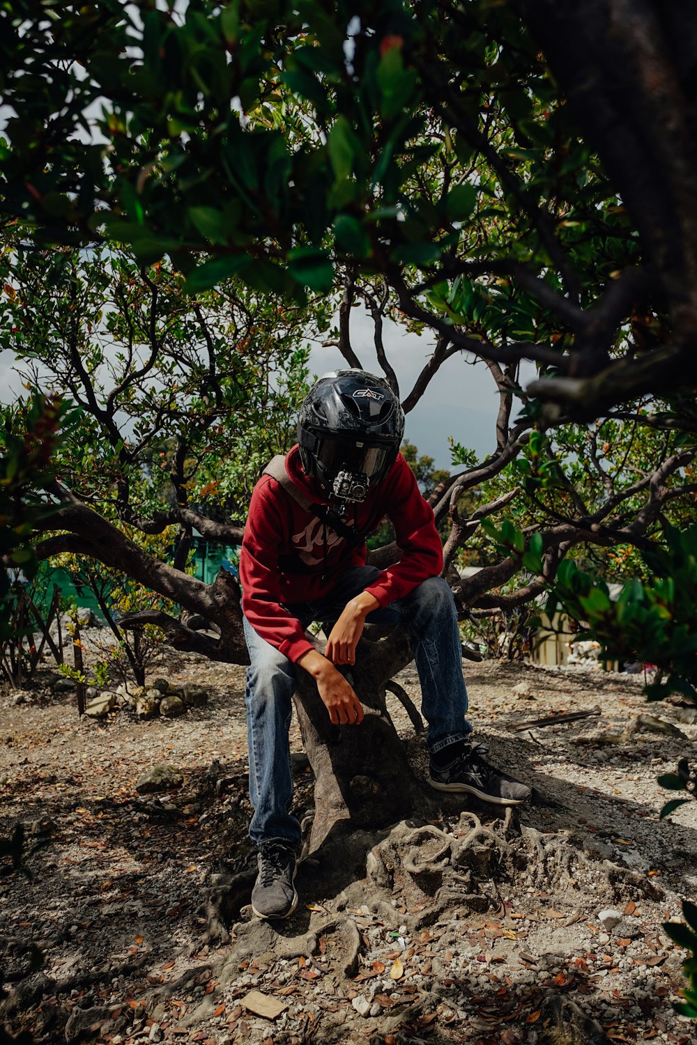 man in red jacket and gray pants wearing helmet standing near green trees during daytime