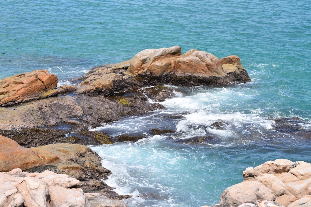 brown rocky shore with ocean waves crashing on rocks during daytime