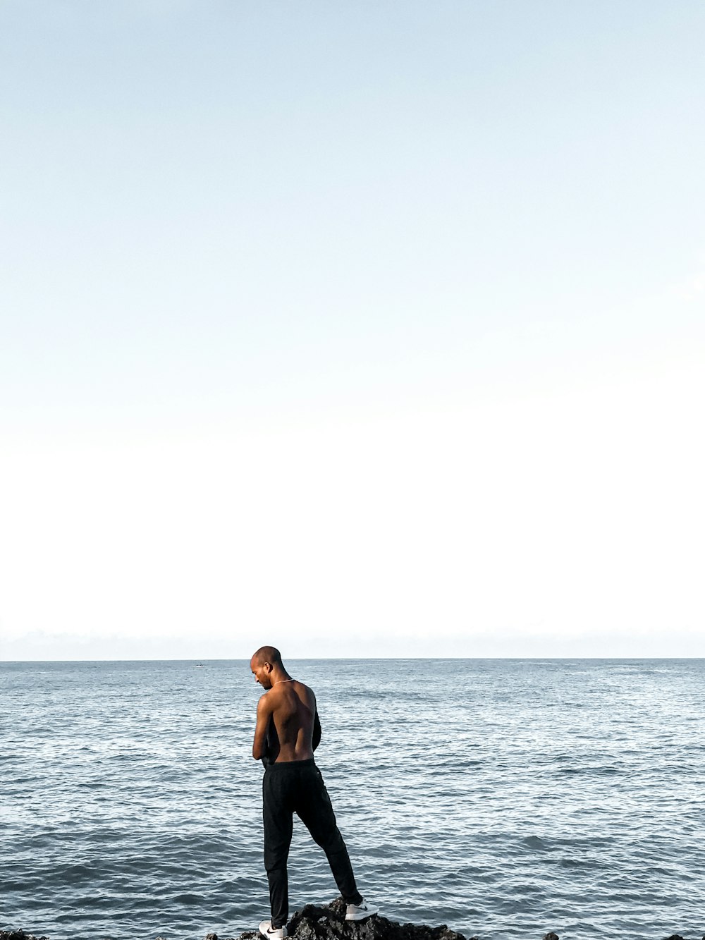 topless man in black shorts standing on sea shore during daytime
