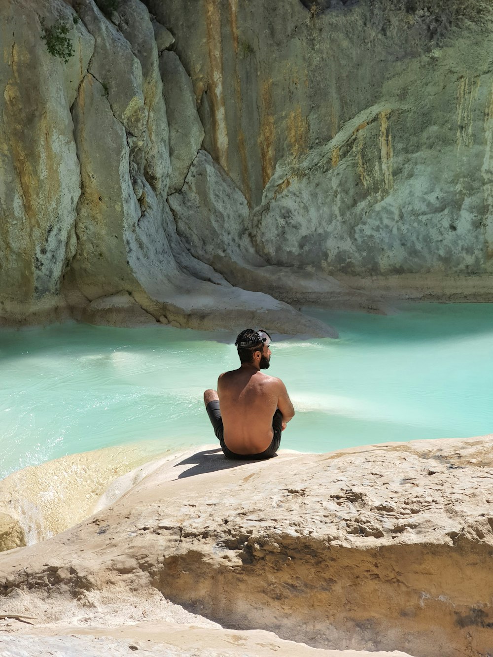 woman in black bikini lying on brown rock near body of water during daytime