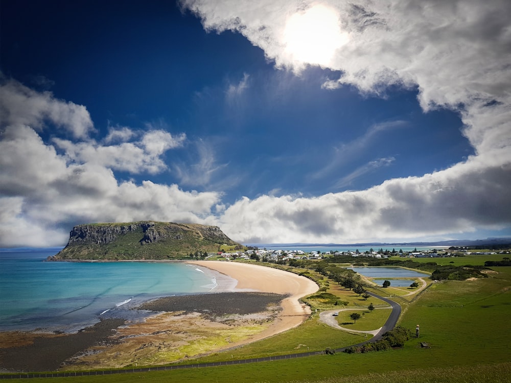 green grass field near body of water under blue sky and white clouds during daytime