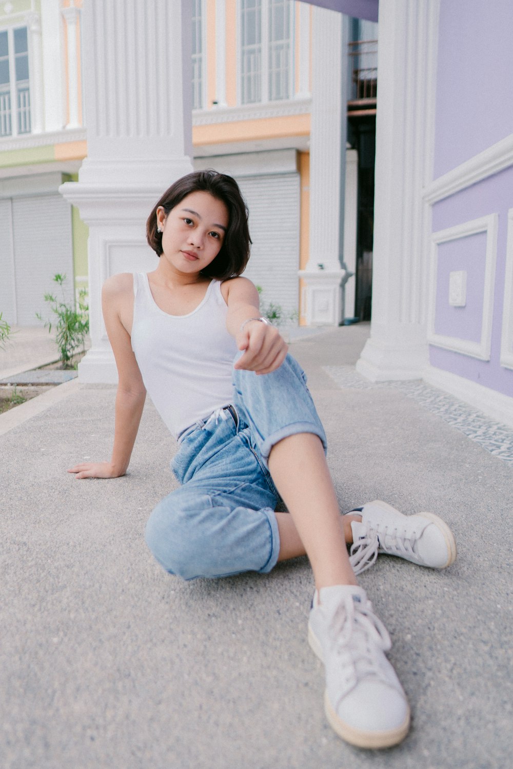 Femme en débardeur blanc et short en jean bleu assise sur un sol en béton gris pendant la journée