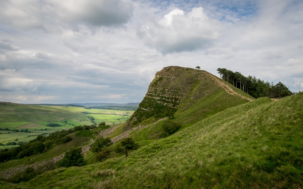 green grass field on hill under cloudy sky during daytime