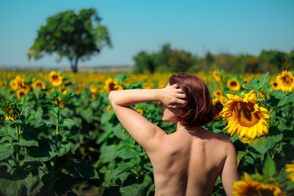 topless woman standing on sunflower field during daytime