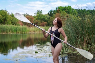 woman in black swimsuit holding paddle standing on river during daytime