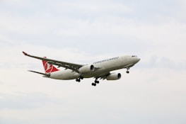 A cargo airplane with the branding 'Turkish Cargo' is flying in the sky. The aircraft is primarily white with red accents on its tail fin. The sky is overcast with light clouds.