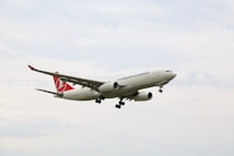 A cargo airplane with the branding 'Turkish Cargo' is flying in the sky. The aircraft is primarily white with red accents on its tail fin. The sky is overcast with light clouds.