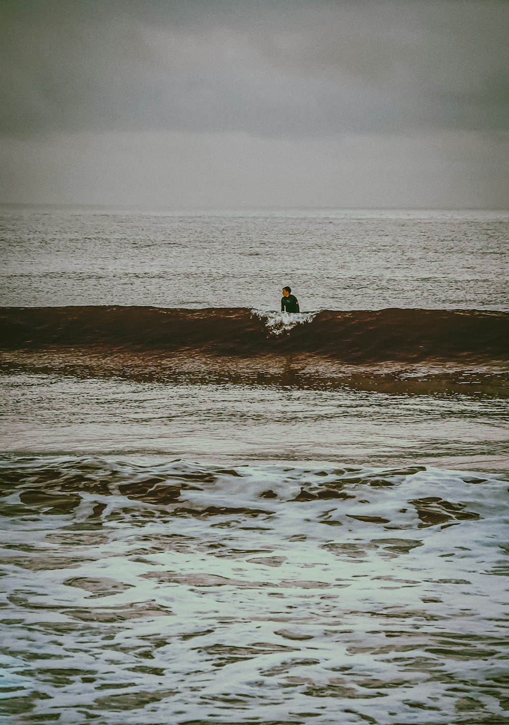 person in white shirt sitting on brown sand near body of water during daytime