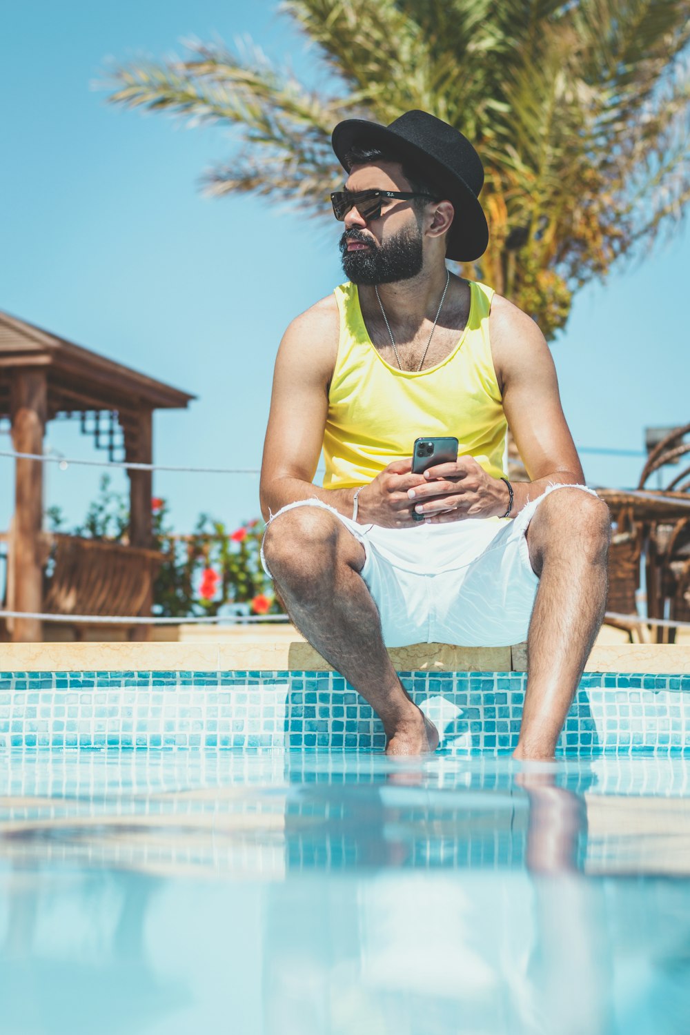 man in yellow tank top and gray shorts sitting on brown wooden bench during daytime