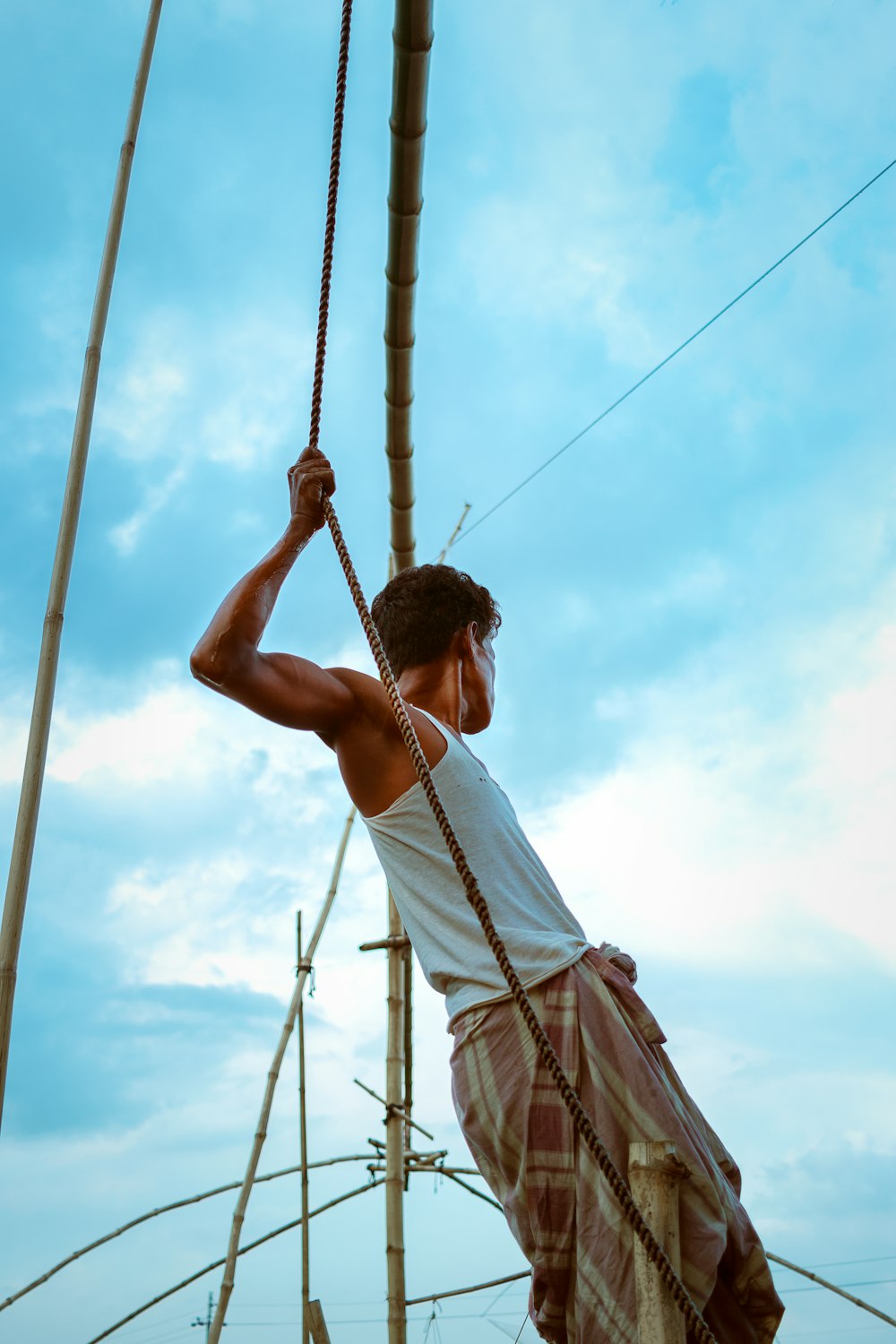 man in white tank top and brown shorts holding rope during daytime