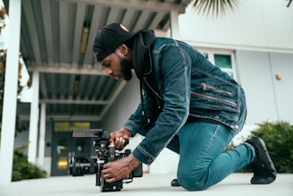 man in black jacket and blue denim jeans holding black dslr camera