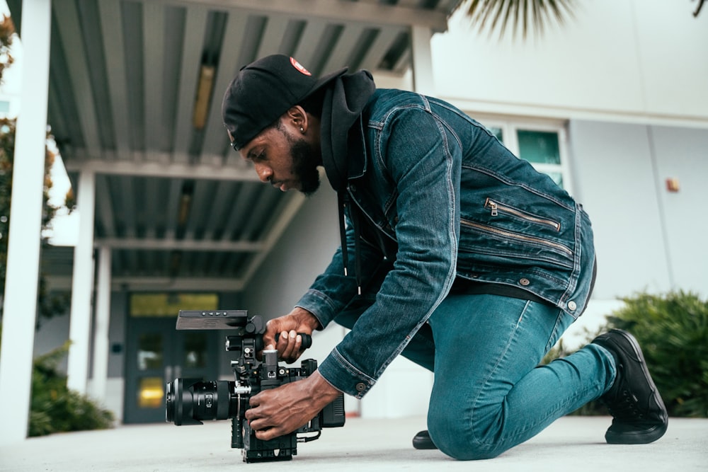 man in black jacket and blue denim jeans holding black dslr camera