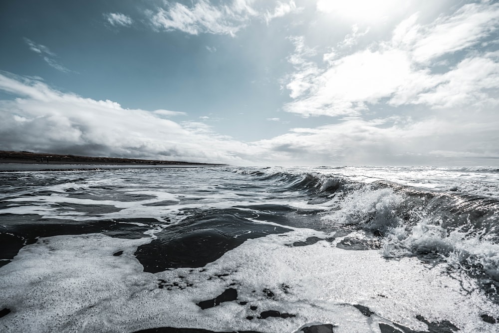 ocean waves crashing on shore under blue and white cloudy sky during daytime