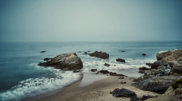 A peaceful stretch of coastline framed by smooth rocks and soft sea foam.