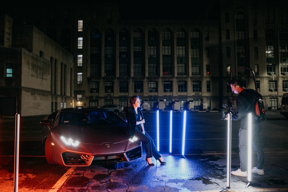 man in black suit standing beside red car during night time