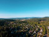 Aerial view of spacious residential plots surrounded by dense green trees under a clear blue sky.