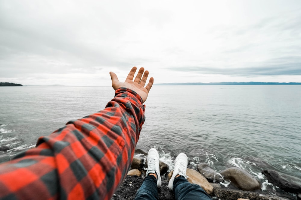 person in orange and blue plaid pants and white sneakers sitting on rock near body of near on near near