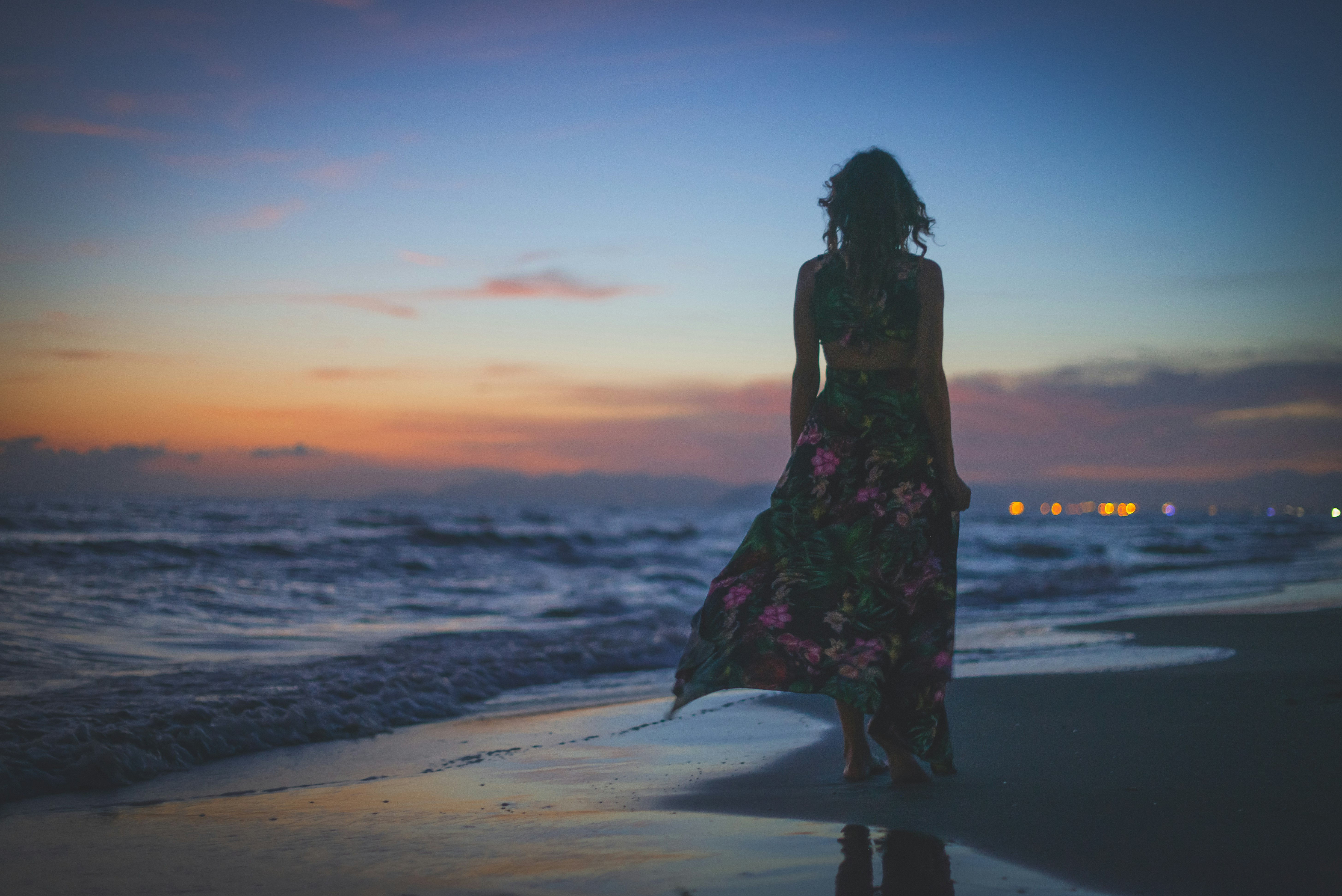 woman in black and red floral dress standing on beach during sunset