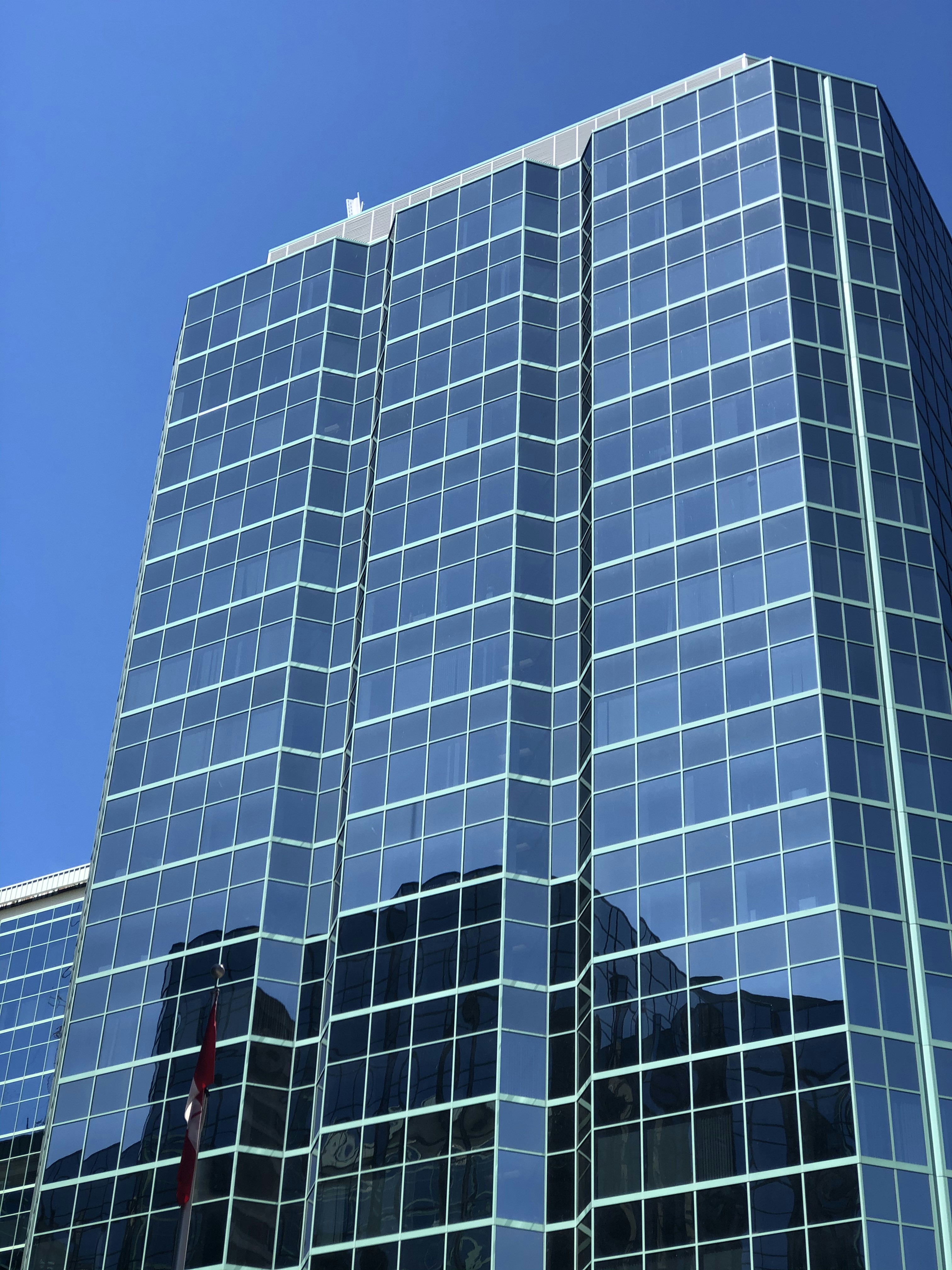 Bright modern government building exterior in clear daylight, clean architecture with maple leaf flag, open civic plaza