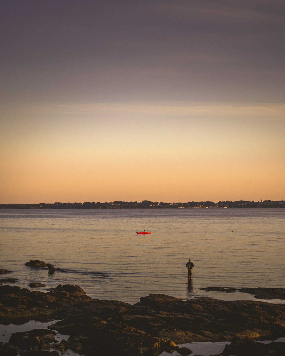 silhouette of person standing on rock near sea during sunset