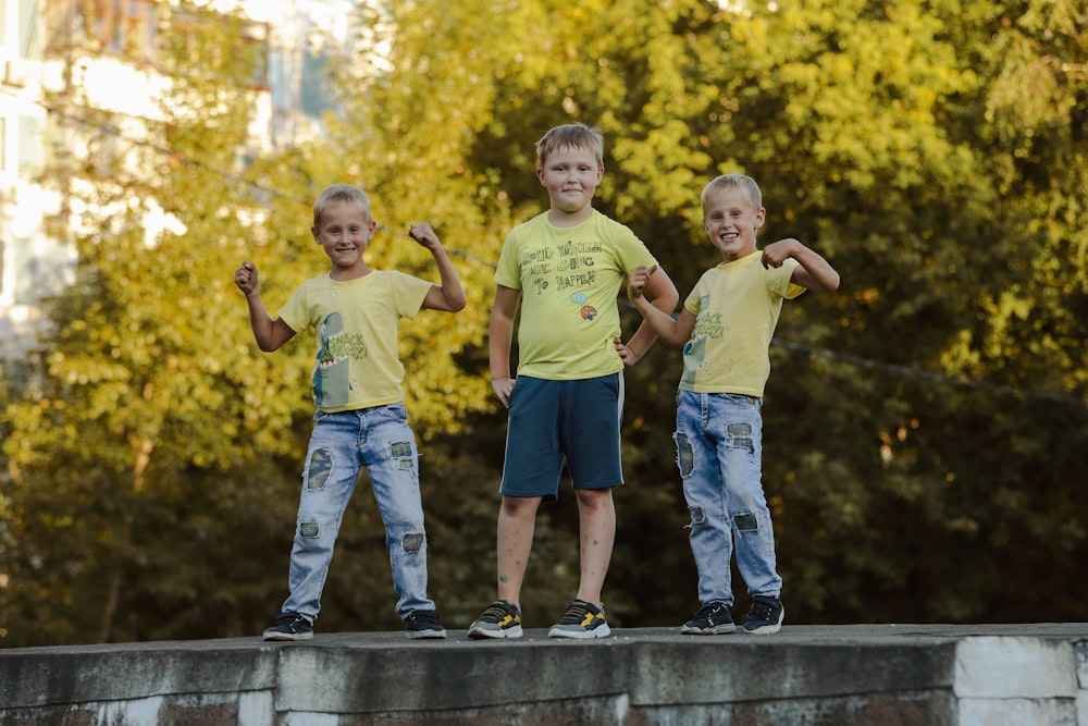 2 boys standing on gray concrete fence during daytime