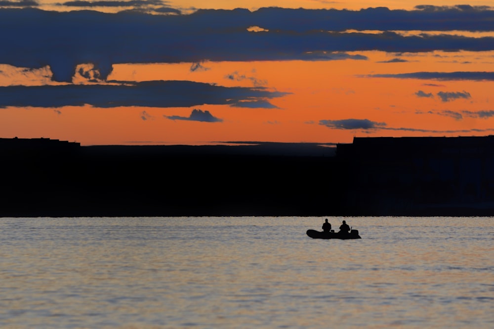 silhouette of two people riding on boat during sunset
