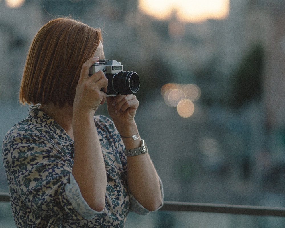 woman in white and blue floral shirt holding black and silver camera