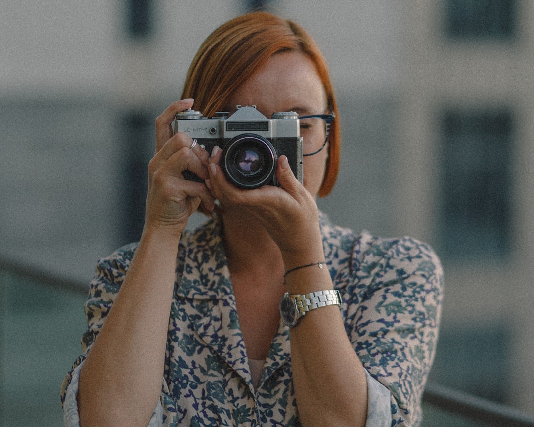 woman in white and blue floral shirt holding black and silver camera