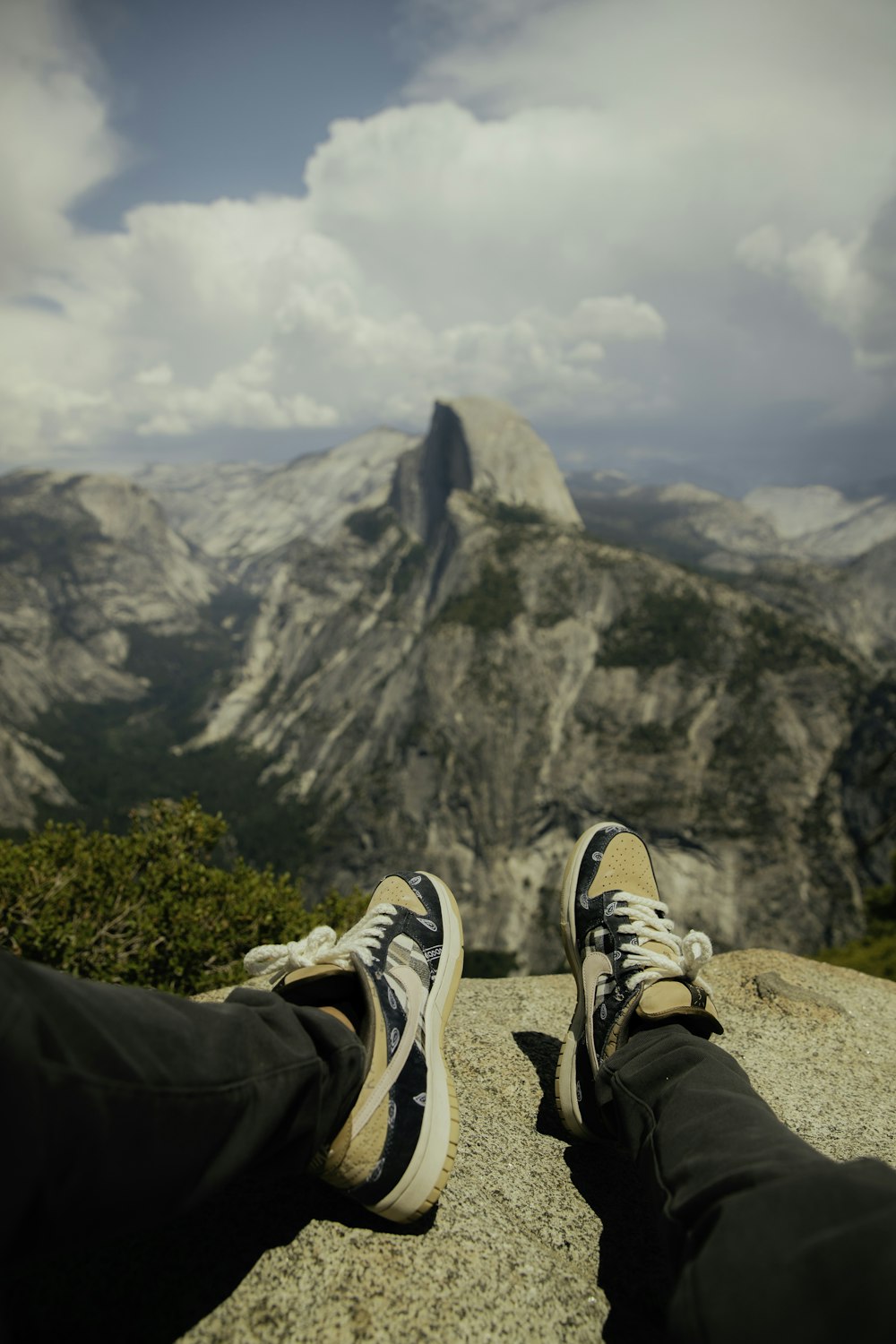 昼間、黒いズボンと茶色と白のスニーカーを履いた人が岩の上に座っている