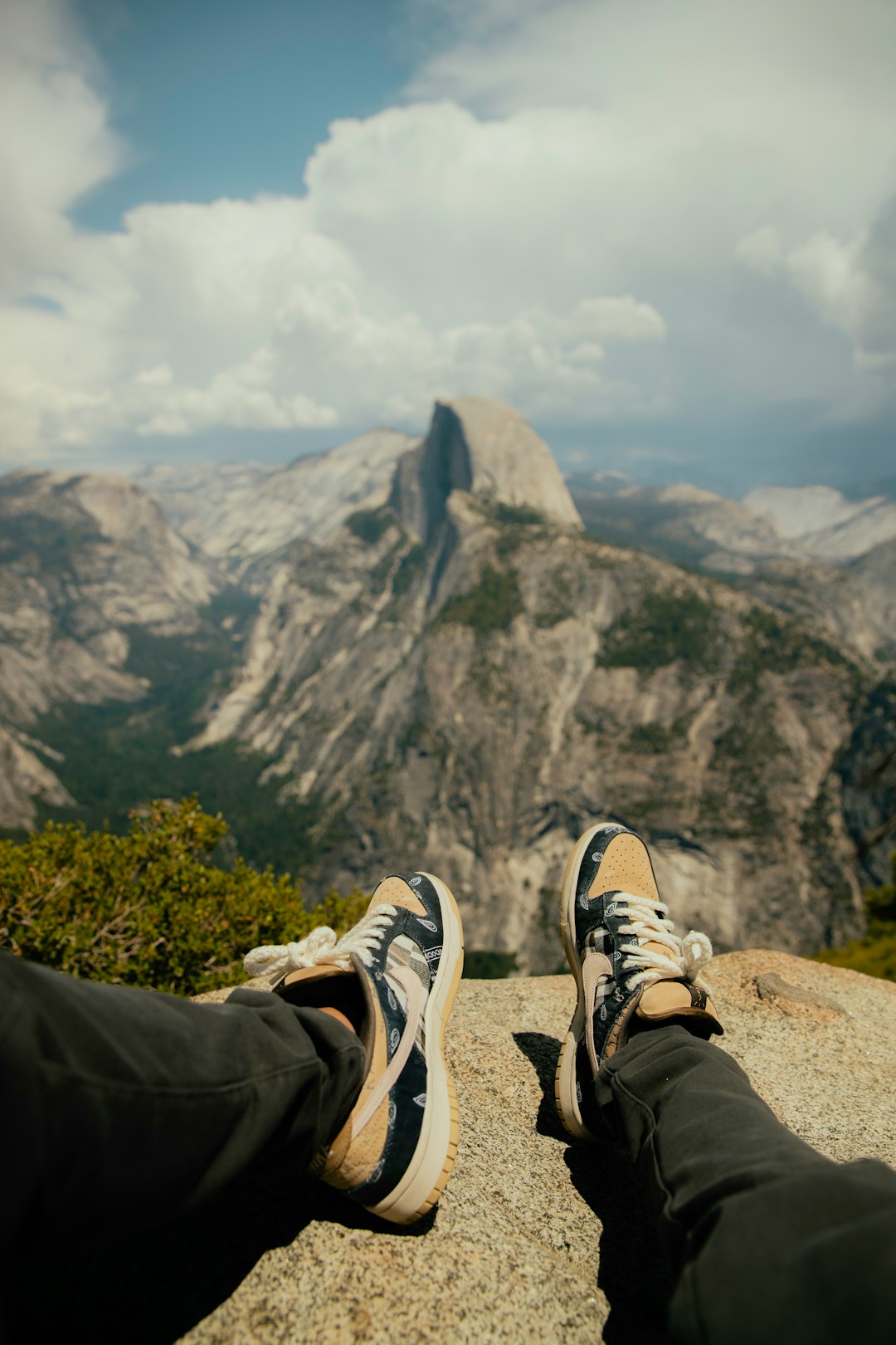 person in black pants and brown and white sneakers sitting on rock during daytime