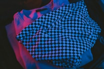 Clothing items illuminated with a vibrant colored light. A piece with a black and white checkerboard pattern lies on top, suggesting a casual or night-out theme.