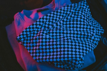 Clothing items illuminated with a vibrant colored light. A piece with a black and white checkerboard pattern lies on top, suggesting a casual or night-out theme.