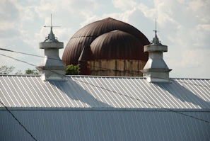 A newly installed custom cupola perched atop a rustic barn under a clear blue sky.