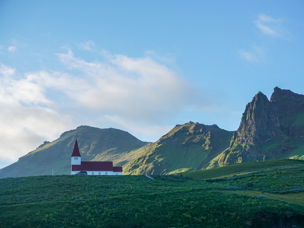 white and red house on green grass field near mountain under white clouds during daytime