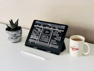 black ipad beside white ceramic mug on white table
