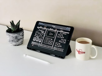 black ipad beside white ceramic mug on white table