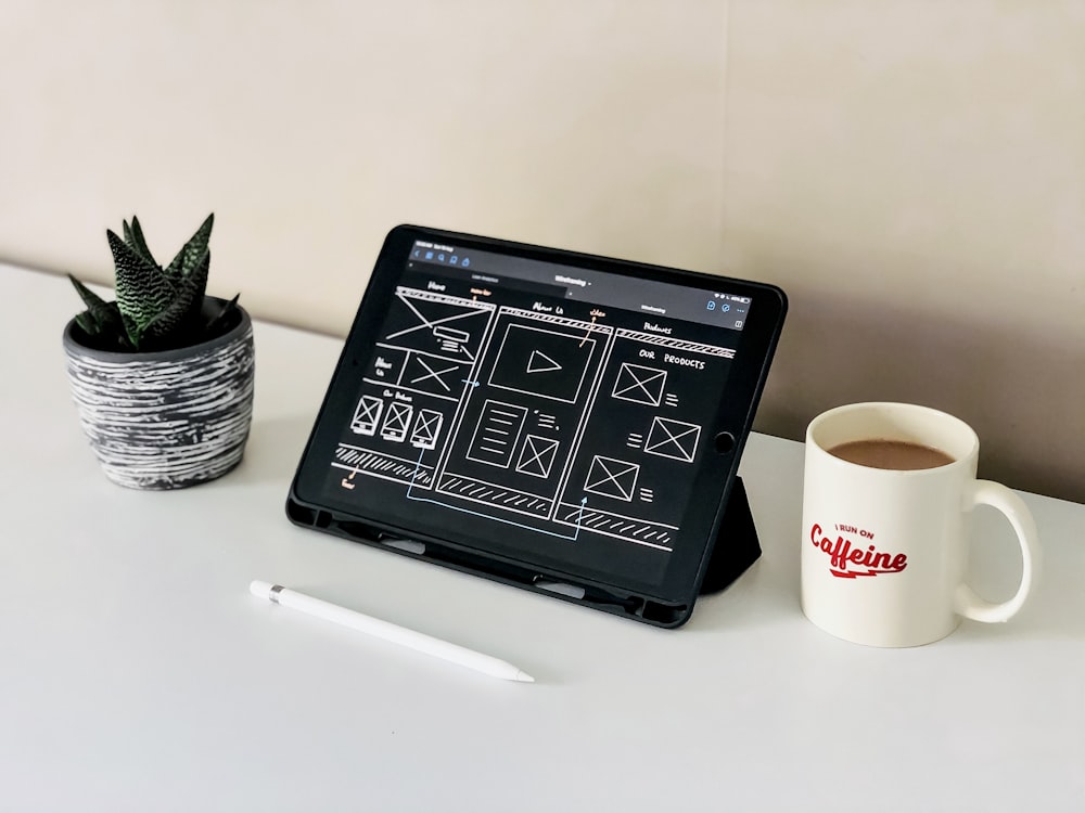 black ipad beside white ceramic mug on white table