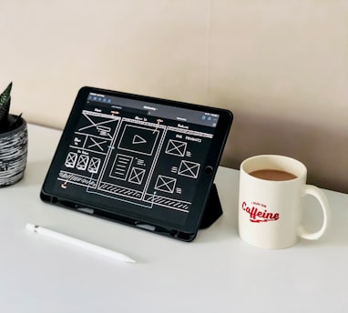black ipad beside white ceramic mug on white table