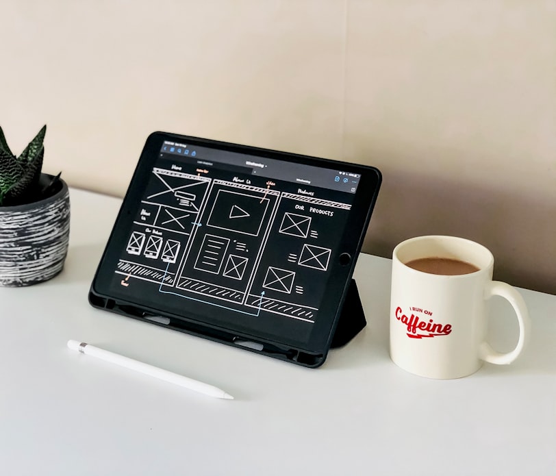 black ipad beside white ceramic mug on white table