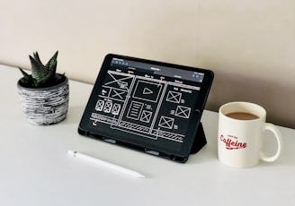 black ipad beside white ceramic mug on white table