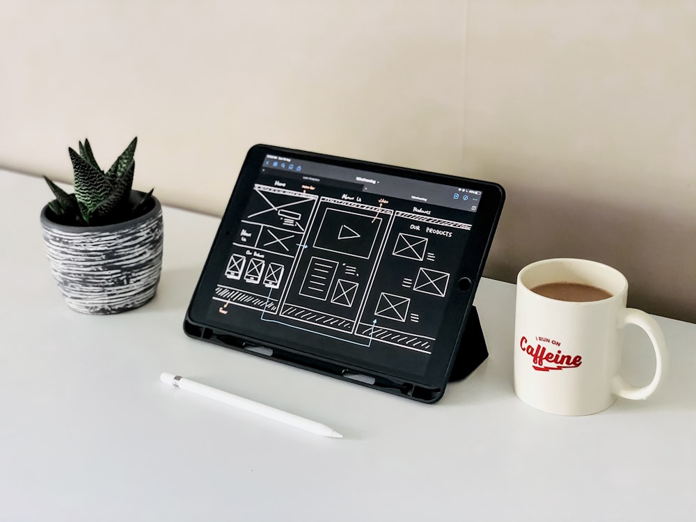 An iPad placed next to a coffee mug and table plant.