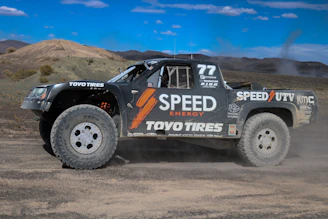 Close-up shot of a race truck kicking up dirt as it navigates rocky terrain.