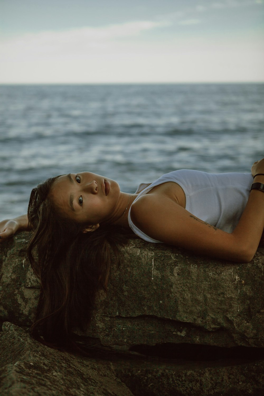 a woman laying on a rock next to the ocean
