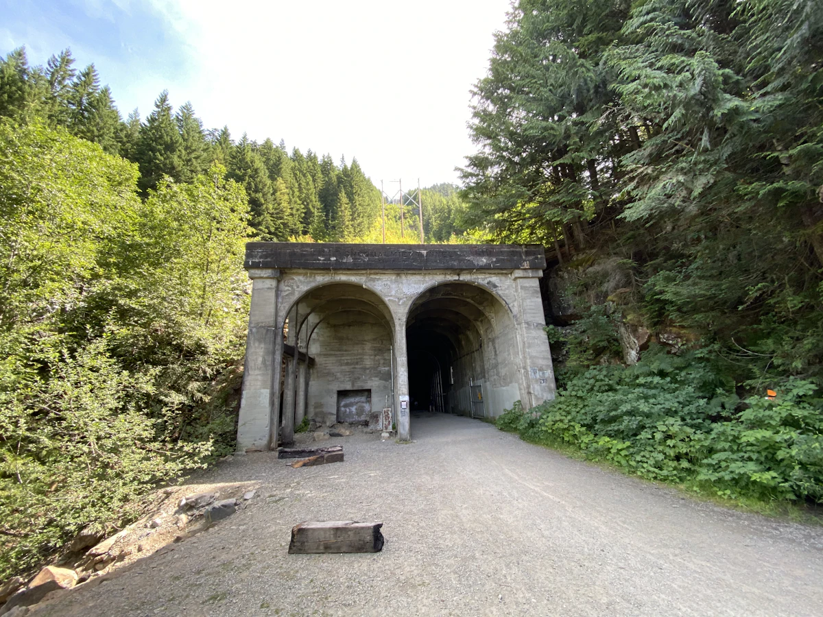 The concrete portal of the Snoqualmie Tunnel at the end of a gravel trail, with forest on both sides