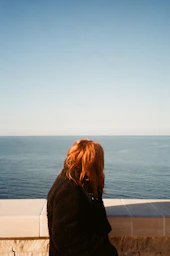 woman in black coat standing near body of water during daytime