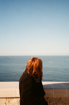 woman in black coat standing near body of water during daytime