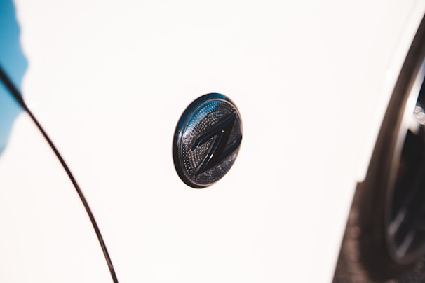 A close-up shot of a car emblem on a white vehicle. The emblem is circular with a dark metallic finish and features a distinctive 'Z' design in the center.